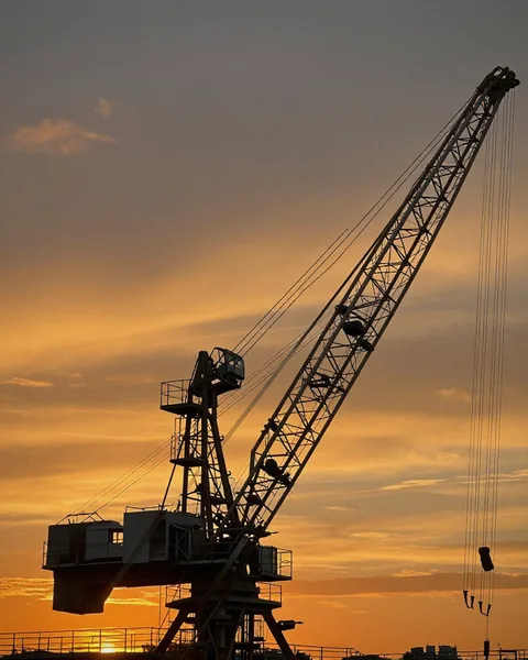 Crane boom and rigging silhouetted against industrial sunset